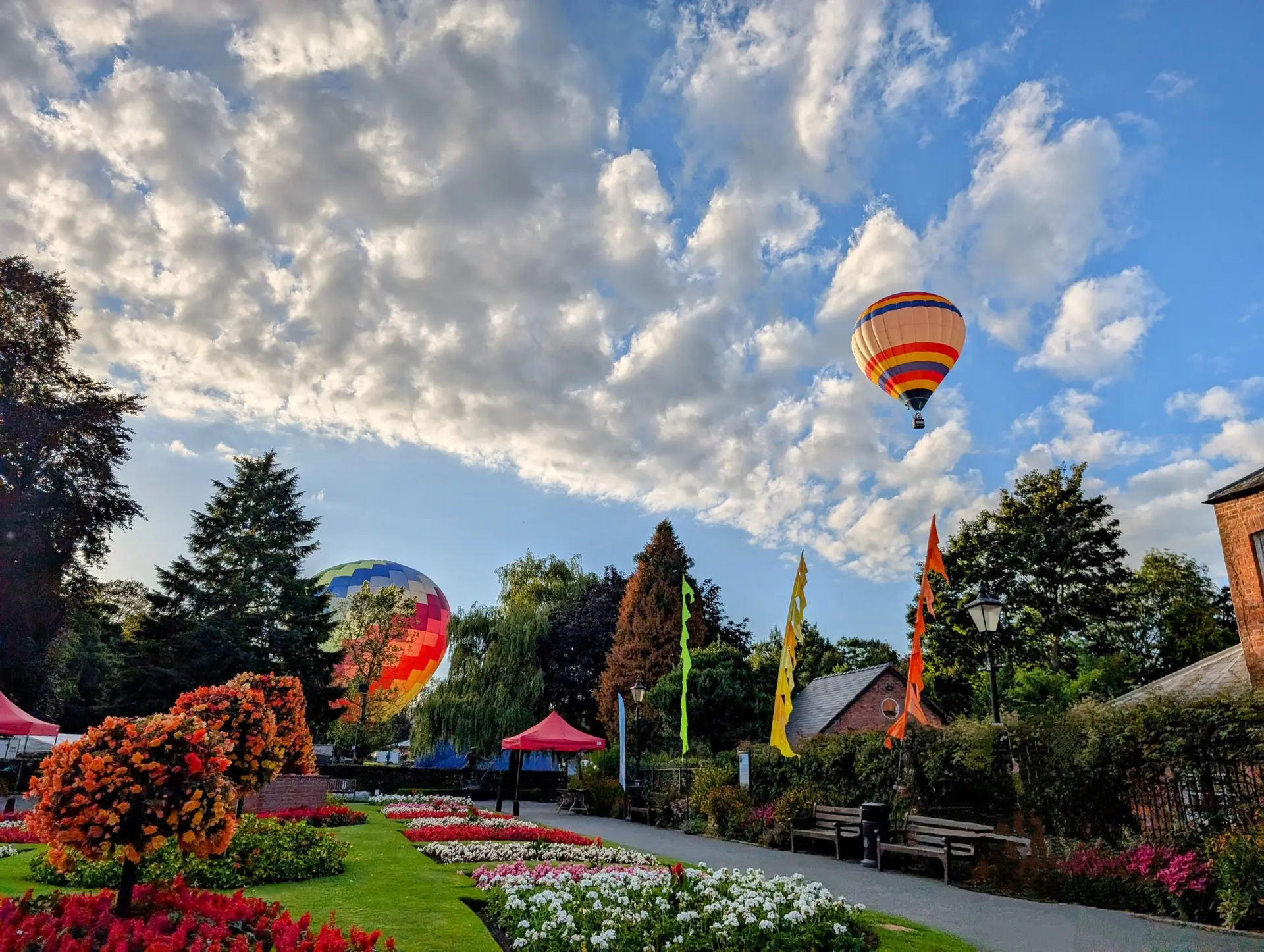 A low-angle view looking directly up at a large blue hot air balloon drifting high against a bright blue sky filled with light, wispy white clouds during the Oswestry Balloon Carnival.