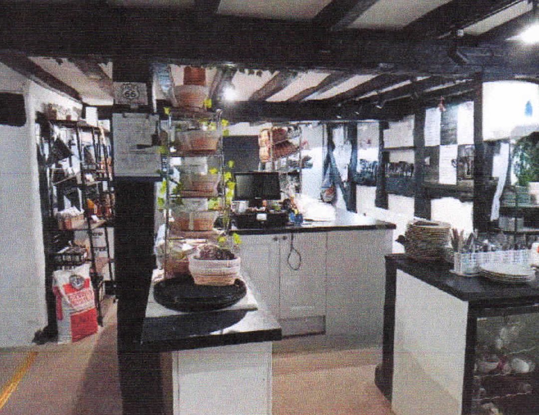 Internal view of a commercial premises highlighting the building's character, including low-profile dark ceiling beams and white walls. The space features built-in white cabinetry, an open counter layout, and versatile floor space suitable for business reconfiguration.