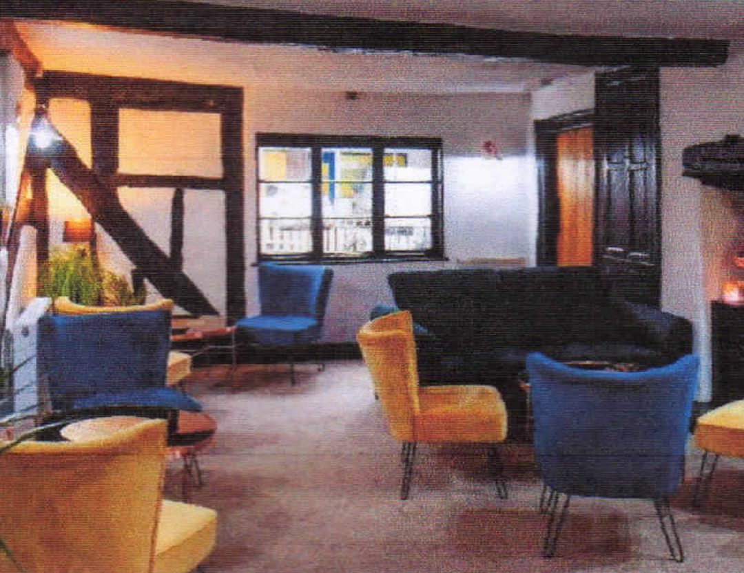 A spacious ground-floor room inside a character building, showcasing historic timber-framed walls and exposed beams. The room features a multi-pane window that brings in natural light, a neutral carpet, and a flexible layout ideal for a lounge, office, or reception area.